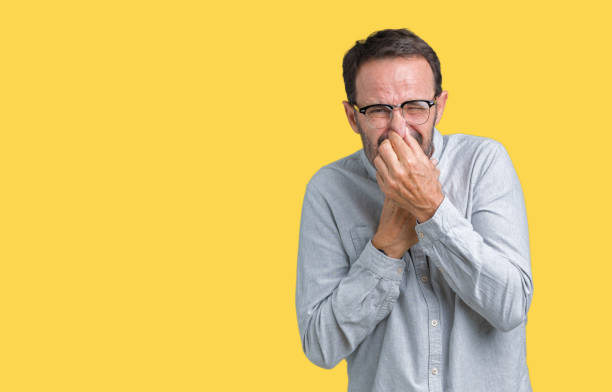 istock Handsome middle age elegant senior man wearing glasses over isolated background smelling something stinky and disgusting, intolerable smell, holding breath with fingers on nose. Bad smells concept. 1097587828