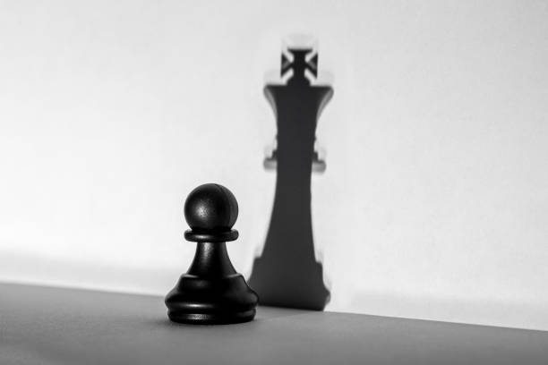 istock Chess pawn standing in a spotlight that make a shadow of king with darkness artistic conversion 1097590738