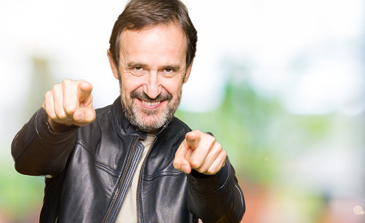 Middle age handsome man wearing black leather jacket Pointing to you and the camera with fingers, smiling positive and cheerful
