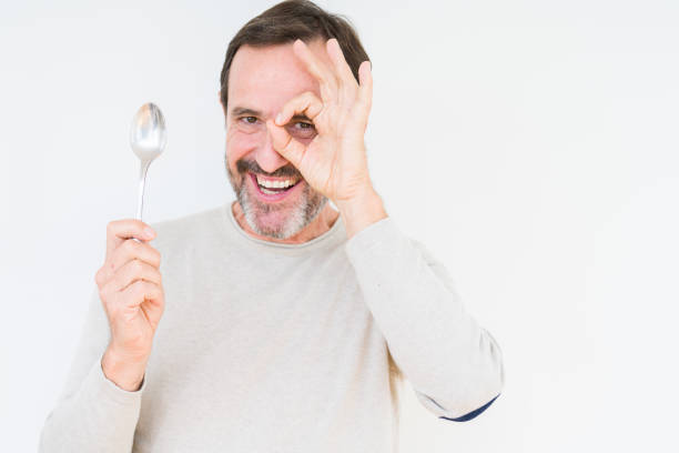 istock Senior man holding silver spoon over isolated background with happy face smiling doing ok sign with hand on eye looking through fingers 1097593984