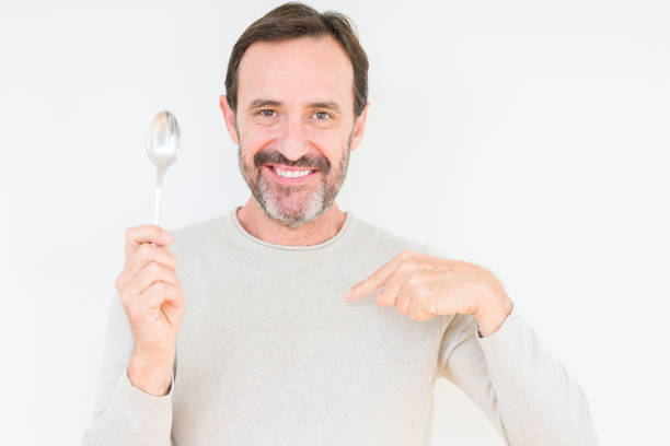 istock Senior man holding silver spoon over isolated background with surprise face pointing finger to himself 1097593990