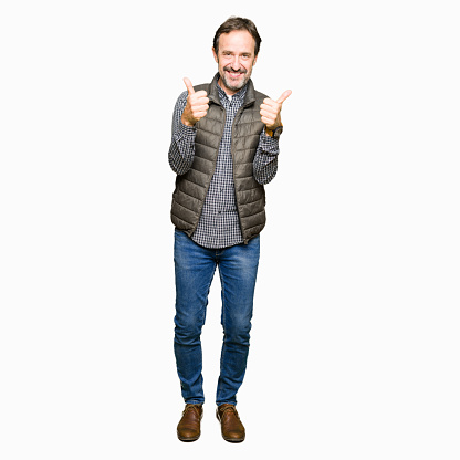 Middle age handsome man wearing winter vest success sign doing positive gesture with hand, thumbs up smiling and happy. Looking at the camera with cheerful expression, winner gesture.