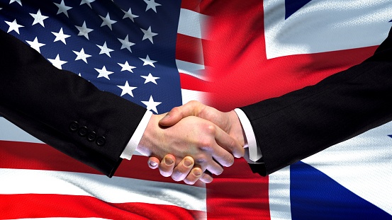 USA and Great Britain handshake, international friendship flag background