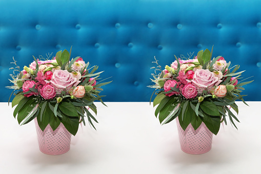 Two identical bouquet of flowers of roses in pink vases on a white table near the turquoise sofa