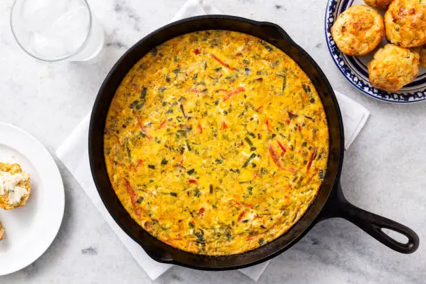 Vegetable egg frittata in cast-iron skillet with homemade jalapeño and cheddar cornbread muffins