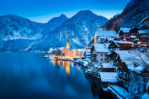 Classic postcard view of famous Hallstatt lakeside town in the Alps with beautiful Hallstattersee in mystical post sunset twilight during blue hour at dusk in winter, Salzkammergut, Austria