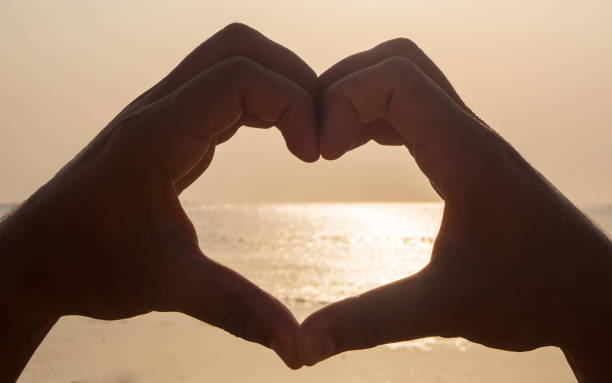 istock Making heart with hands against bright sea sunset and sunlight on the water 1097663646
