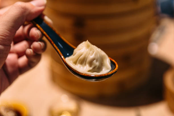 istock Xiao Long Bao (Soup Dumpling) in spoon with blur bamboo streamer basket in background. 1097665094