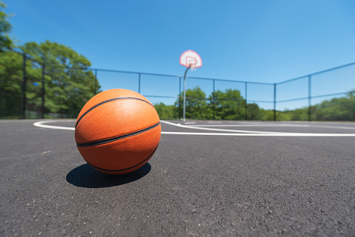 A low wide angle view of a basketball on an outdoor basketball court.