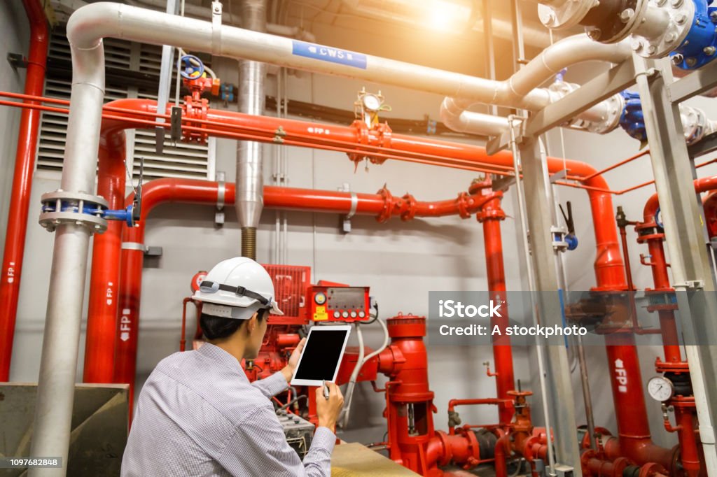 Engineer with tablet check red generator pump for water sprinkler piping and fire alarm control system. Fire - Natural Phenomenon Stock Photo