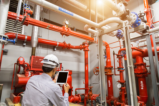 A mature Caucasian engineer is standing in a heating plant and using his tablet to perform a system check.
