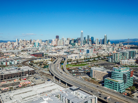 Aerial view of the San Francisco Skyline as the 280 Freeway empties into the city. Iconic skyscrapers fill the horizon. Mission Bay and the Bay Bridge are visible.