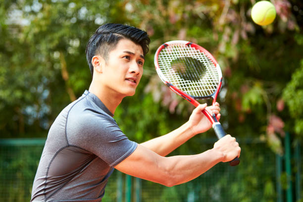 young asian male player playing tennis young asian male tennis player hitting ball with a backhand backhand stroke stock pictures, royalty-free photos & images