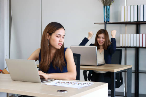 young angry envious asian business woman looking successful competitor colleague in office. - inveja imagens e fotografias de stock