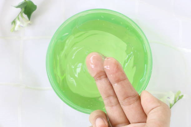 Top view of close up woman finger applying aloe vera gel cream in green container on white fabric background Top view of close up woman finger applying aloe vera gel cream in green container on white fabric background aloe plant alternative medicine body care stock pictures, royalty-free photos & images