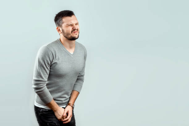 un hombre joven y atractivo siente dolor en su ingle, brazos cruzados entre sus piernas. experimentar dolor, problemas masculinos, potencia. - orinar fotografías e imágenes de stock