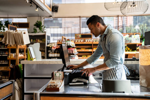 latin american male cashier at the supermarket looking something on system looking serious - store retail supermarket checkout counter imagens e fotografias de stock