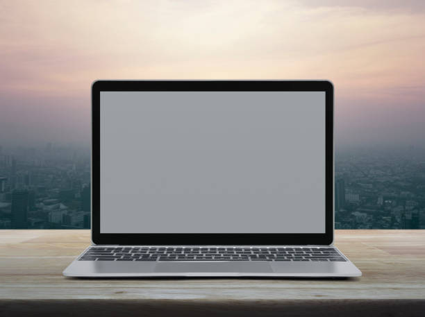 istock Modern laptop computer with blank grey screen on wooden table over office city tower and skyscraper at sunset sky, vintage style 1097712648