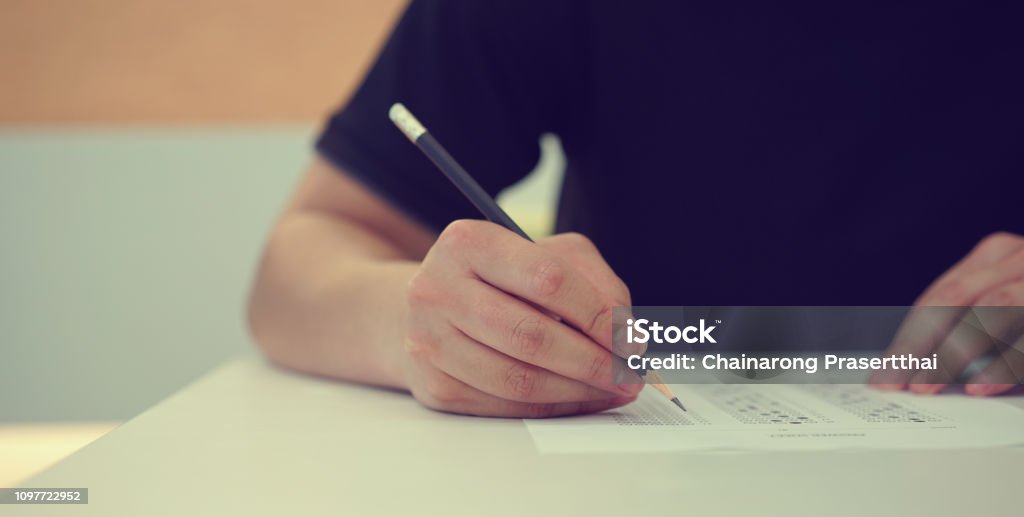 close up high school student man hand writing by marking choices on answer sheet paper for final examination test in classroom concept Educational Exam Stock Photo