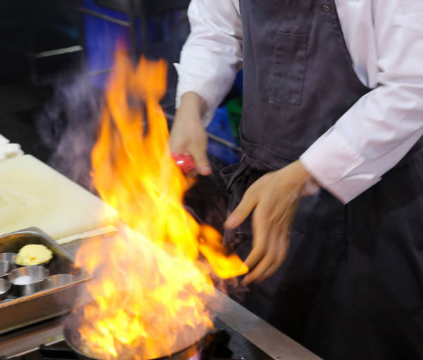 Chef in restaurant kitchen at stove with pan, doing flambe on food