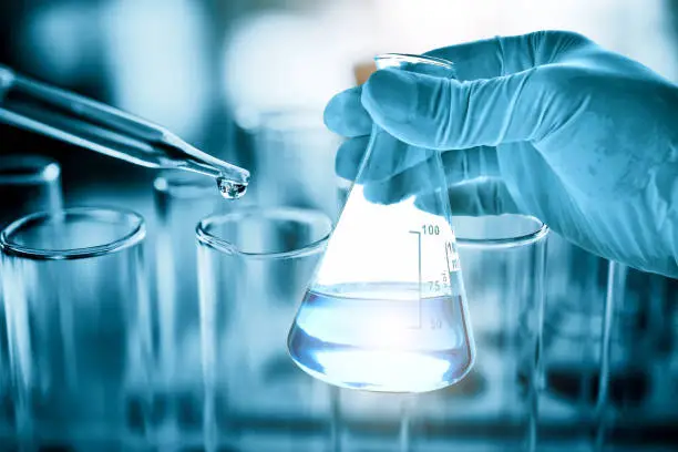 Photo of hand of scientist holding flask with lab glassware in chemical laboratory background, science laboratory research and development concept