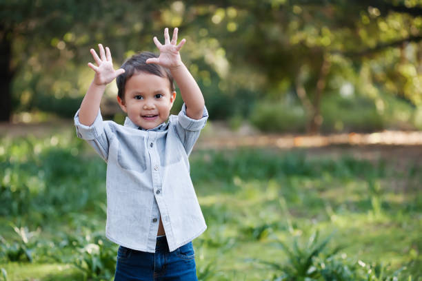 giovane bambino che usa le mani per esprimersi, in piedi all'aperto in un campo verde che sembra felice. - child exercising little boys toddler foto e immagini stock