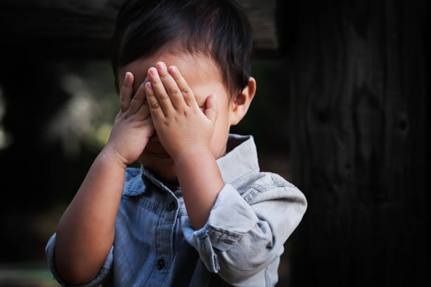 a young boy of toddler age covering his face with hands, showing signs of distress, fear and dissapointment. - disaffection imagens e fotografias de stock