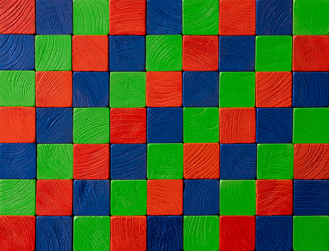 Many square wood grain textured red, green and blue wooden blocks stacked up on top of each other creating a wood grained RGB abstract color background that could represent square pixel related concepts.