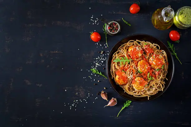 Photo of Italian pasta. Spaghetti with meatballs and parmesan cheese in black plate on dark rustic wood background.  Dinner. Top view. Slow food concept