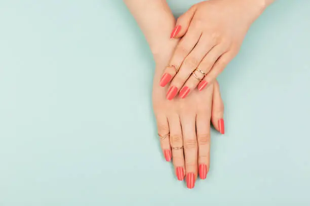 Manicure in trendy coral color. Woman hands on blue background. Color of 2019 year concept. Summer vibes. Copy space for your text.