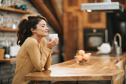 Young woman enjoying in a smell of fresh coffee in the kitchen.