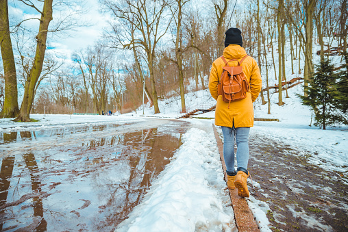 woman walking by city park passing puddles around. melting snow. snow is coming