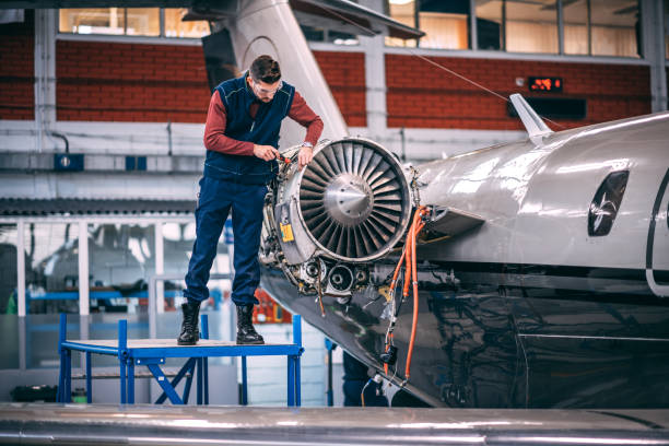istock Aircraft mechanic using a screwdriver to open up a panel on a jet engine of a small aircraft while standing on a raised platform in a maintenance hangar 1097755676
