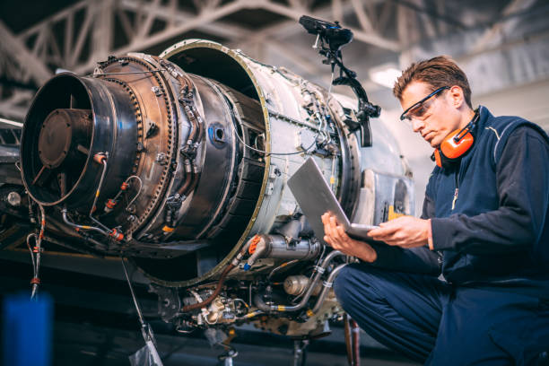 Aircraft engineer in a hangar using a laptop while repairing and maintaining an airplane jet engine Aircraft engineer in a hangar holding laptop computer while repairing and maintaining a jet engine. air vehicle stock pictures, royalty-free photos & images