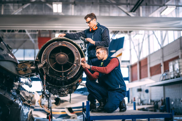 Two aircraft mechanics repairing an uncovered jet engine of a small airplane stock photo