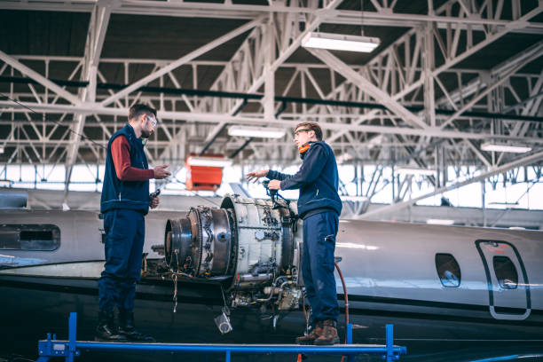 istock Two airplane mechanics standing on a raised work platform and having a conversation about something while working on a partially disassembled jet engine of a small airplane in a maintenance hangar 1097759550