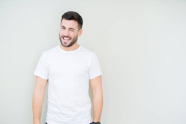 Young handsome man wearing casual white t-shirt over isolated background winking looking at the camera with sexy expression, cheerful and happy face. Young handsome man wearing casual white t-shirt over isolated background winking looking at the camera with sexy expression, cheerful and happy face. young man wink stock pictures, royalty-free photos & images