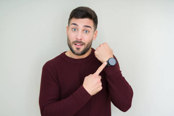 young handsome man wearing a sweater over isolated background in hurry pointing to watch time, impatience, upset and angry for deadline delay - clock face fotos imagens e fotografias de stock
