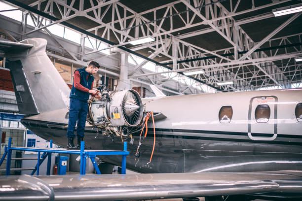 istock Airplane mechanic standing on a raised work platform, unscrewing a piece of inner paneling of a small jet engine in an aircraft maintenance hangar 1097762458