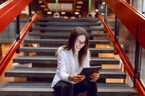 étudiante souriante avec les lunettes et les cheveux bruns avec tablette en position assise sur les marches. - women computer home interior brown hair photos et images de collection