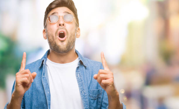 istock Young handsome man wearing sunglasses over isolated background amazed and surprised looking up and pointing with fingers and raised arms. 1097765102