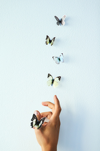 Studio shot of an unrecognizable person releasing butterflies into the air against a grey background