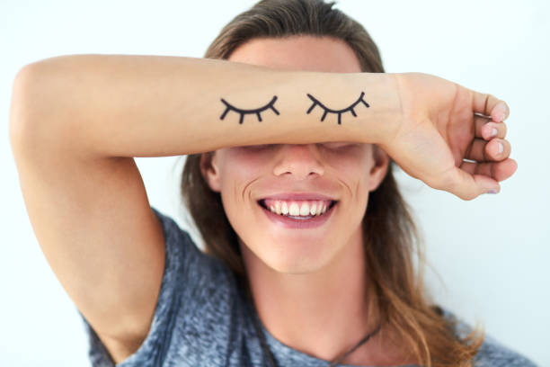 I choose to see what makes me happy Studio shot of a young man raising his arm with eyelash illustrations on in front of his eyes forearm tattoos men stock pictures, royalty-free photos & images