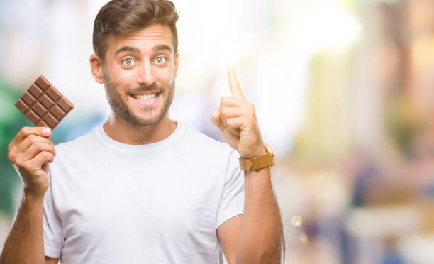 istock Young handsome man eating chocolate bar over isolated background surprised with an idea or question pointing finger with happy face, number one 1097765778
