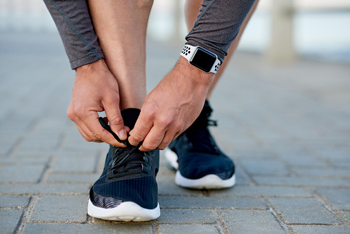 Closeup shot of an unrecognizable man tying his shoelaces while exercising outdoors
