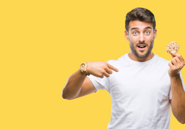 istock Young handsome man eating chocolate chips cookie over isolated background with surprise face pointing finger to himself 1097768238
