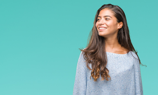 Young beautiful arab woman wearing winter sweater over isolated background looking away to side with smile on face, natural expression. Laughing confident.