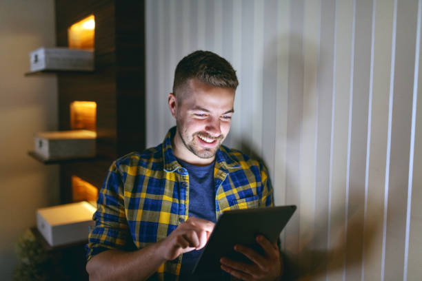 istock Smiling employee dressed in plaid shirt using tablet while leaning on wall in his office late at night. 1097776538