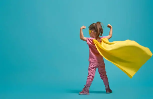 Little child playing superhero. Kid on the background of bright blue wall. Girl power concept. Yellow, pink and  turquoise colors.