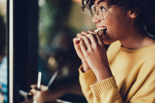 Cropped portrait of beautiful young woman. She eating frest sandwich for breakfast in cafe